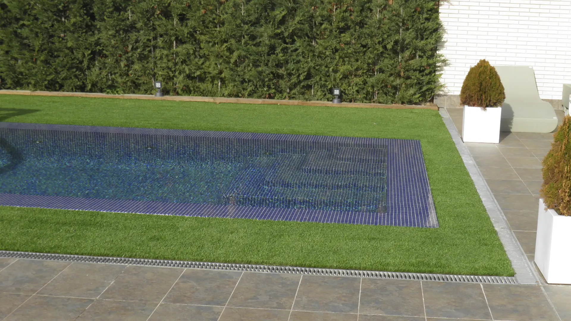 Una imagen lateral de la piscina donde se aprecia el brillo del agua en toda la superficie de la piscina incluyendo los bordes, los cuales quedan pocos milímetros bajo el agua permitiendo su desbordamiento.